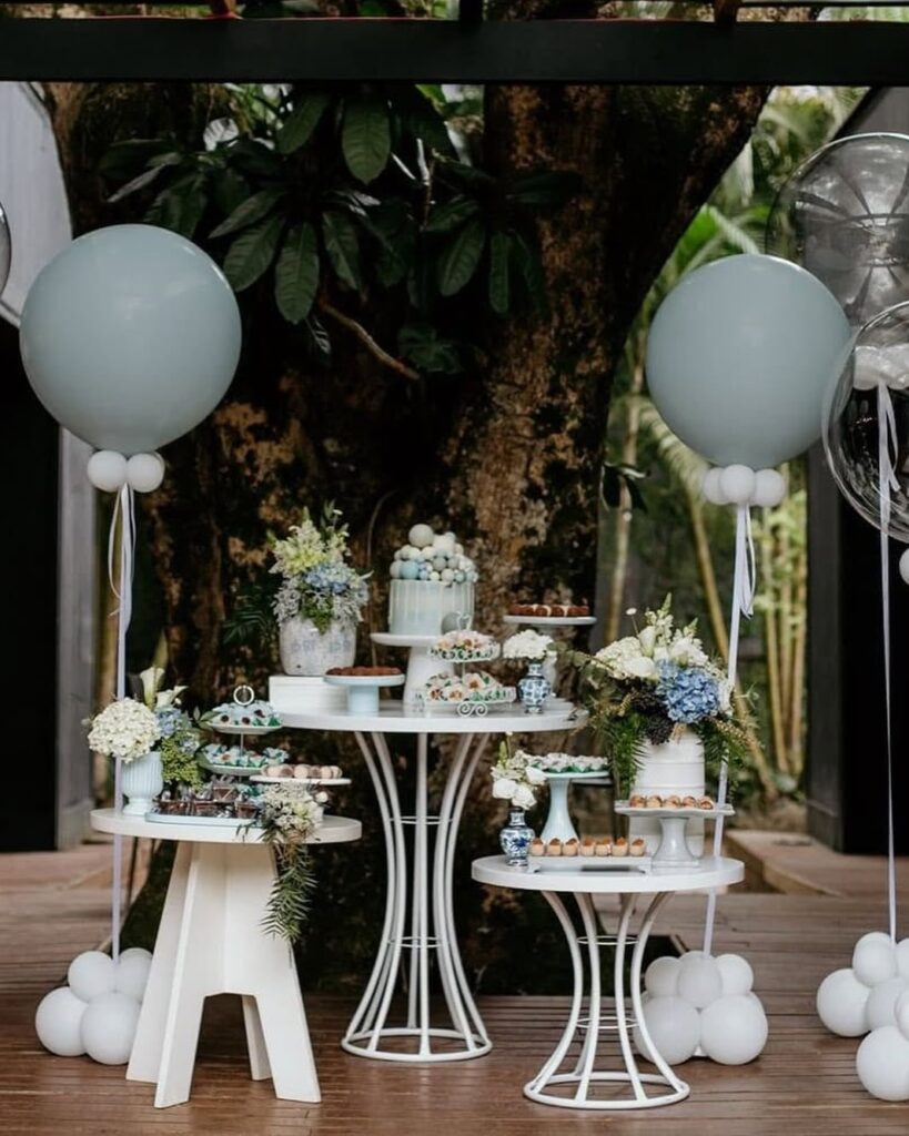 Mesa de doces montada ao ar livre com bolo, balões e suportes do acervo